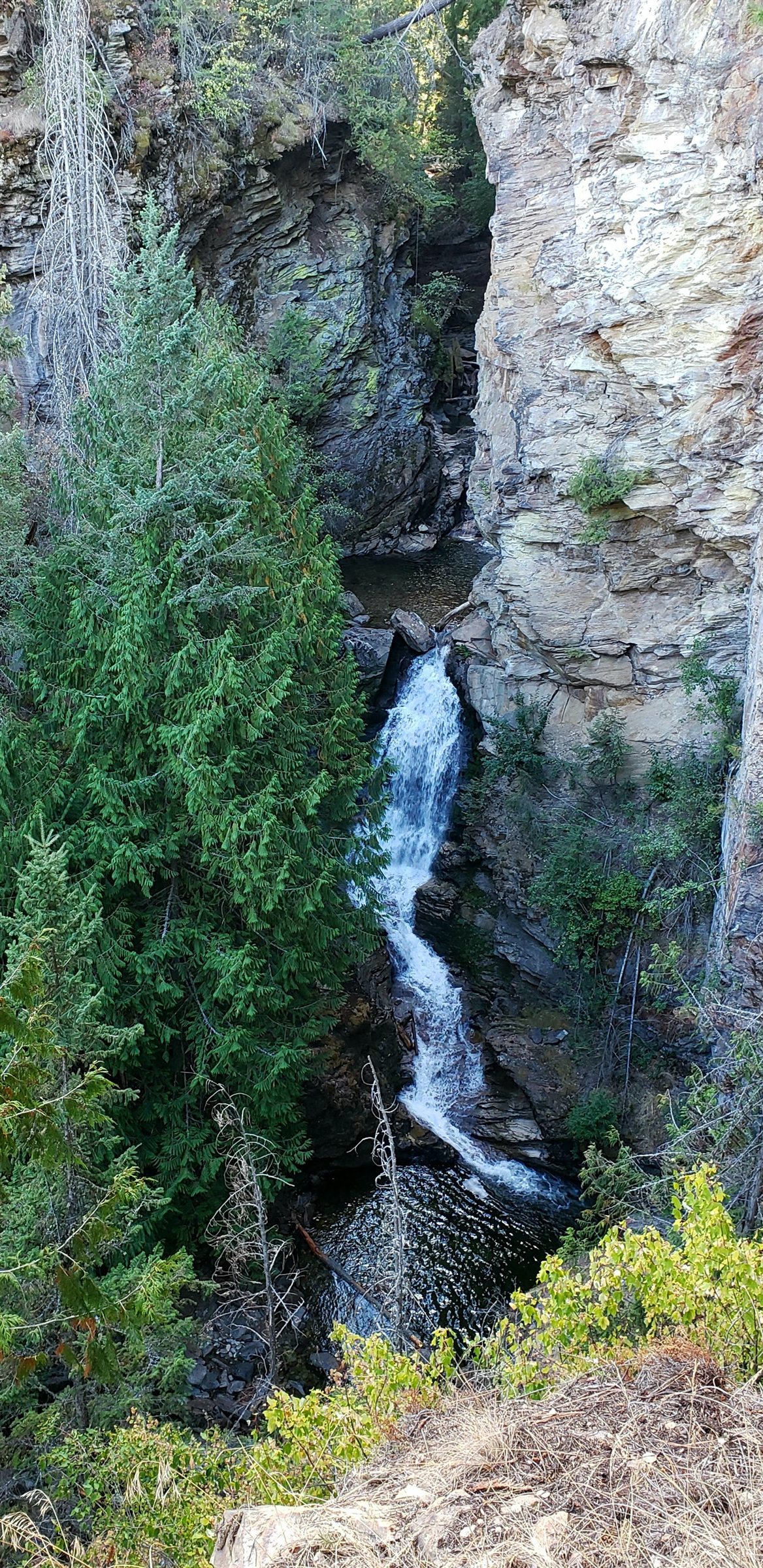 A tall waterfall dropping through a narrow forested rock canyon