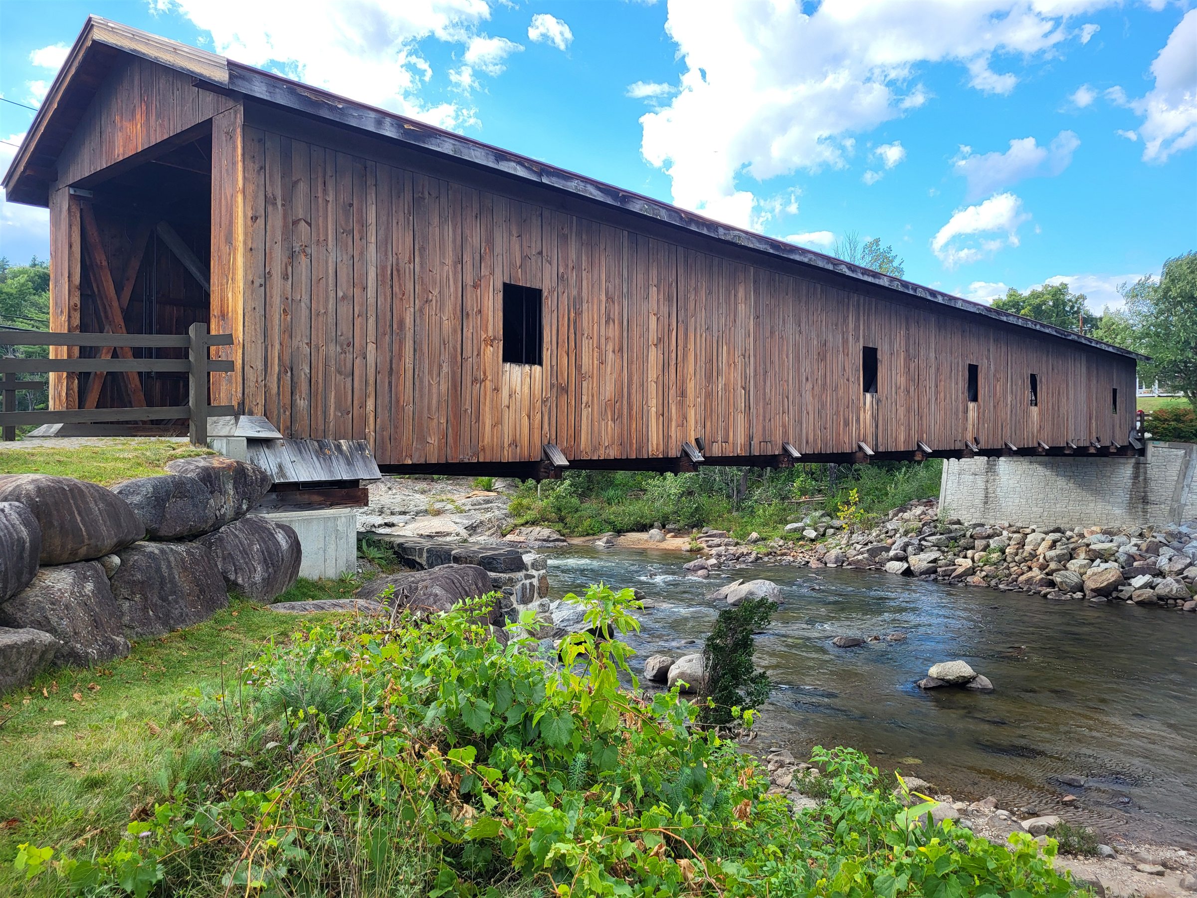 A long wooden covered bridge crossing a rocky river