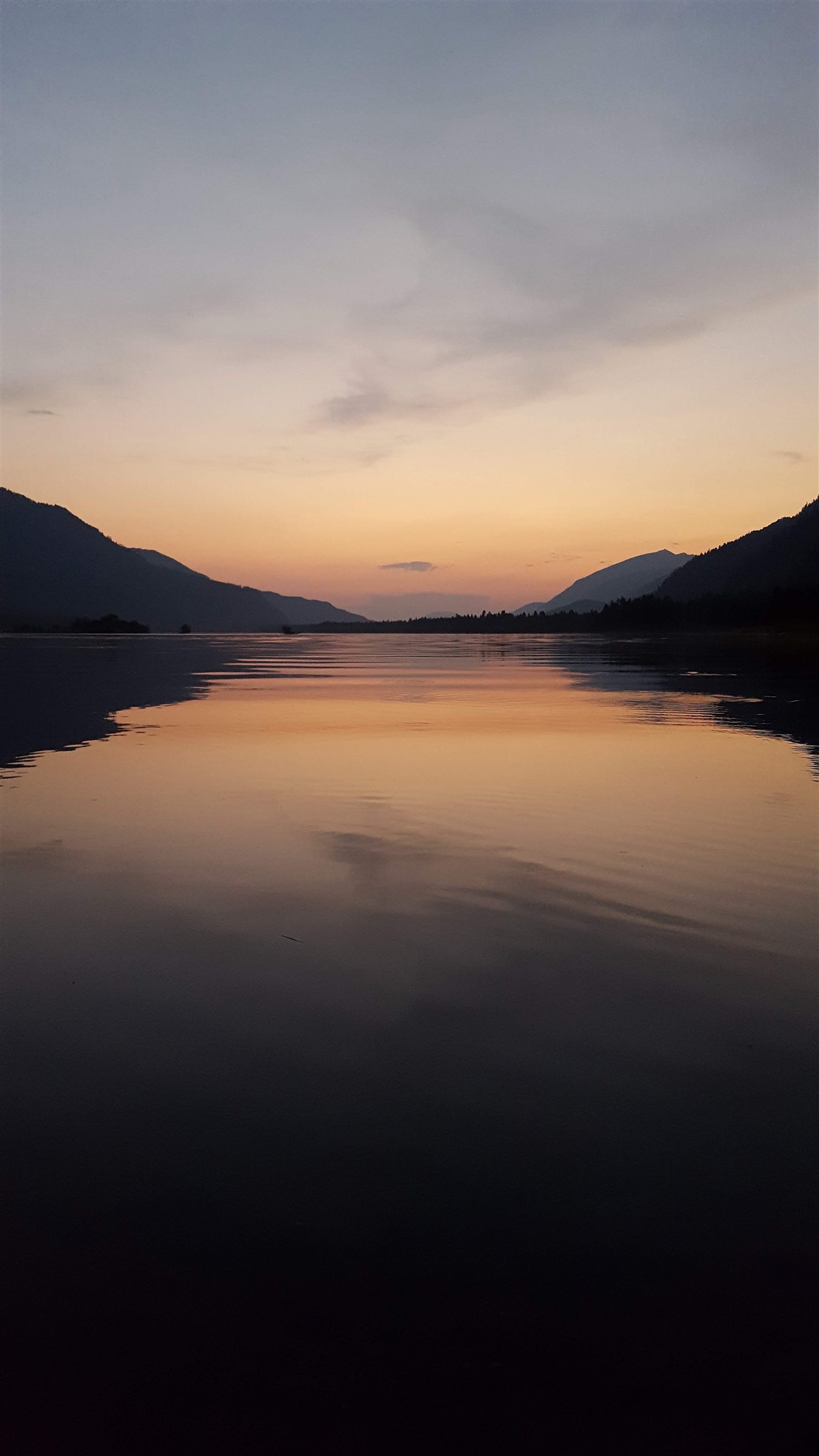 A calm river reflecting a warm sunset between dark mountain silhouettes