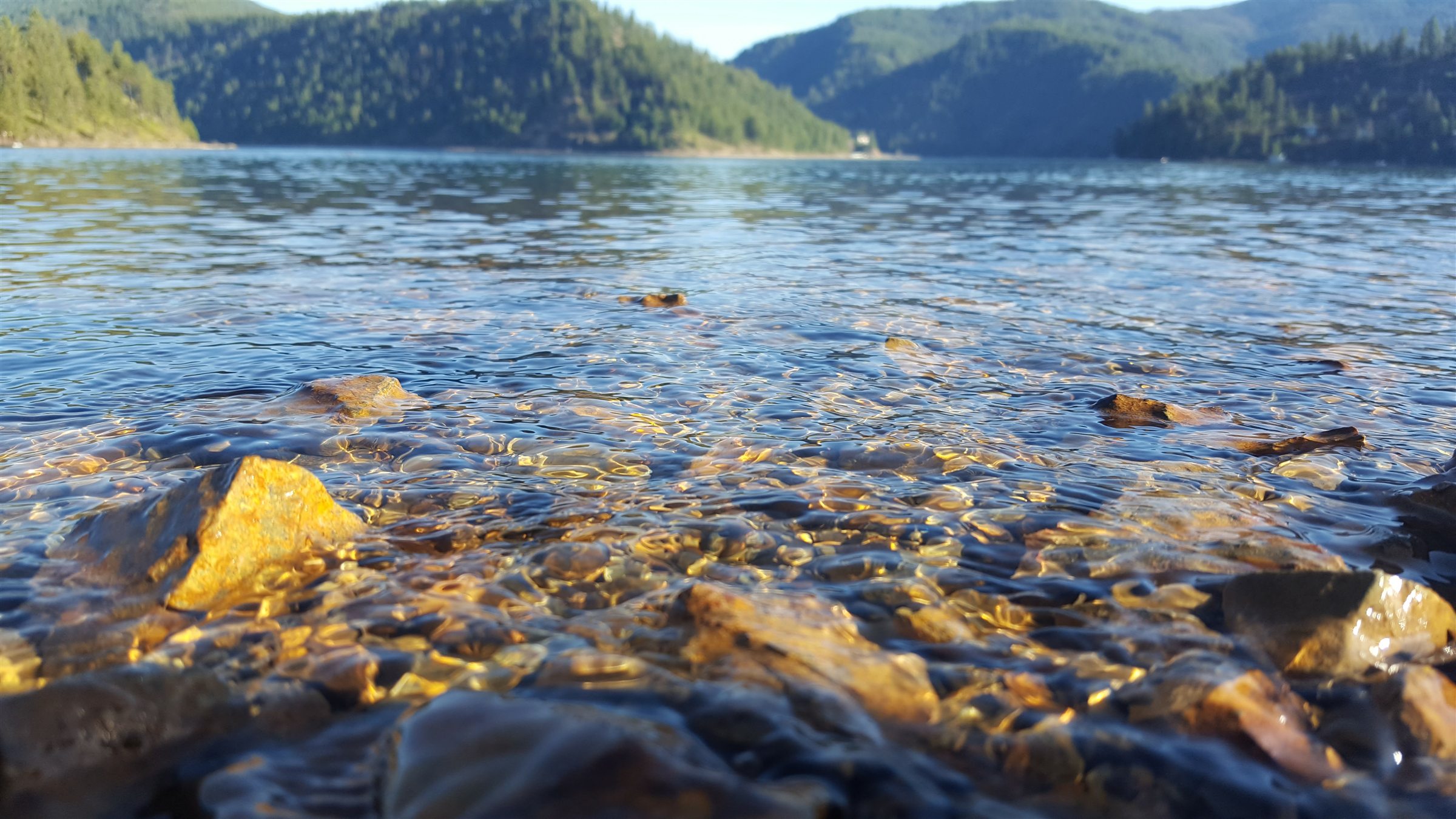 Clear sunlit water and colorful stones along a mountain lake shoreline
