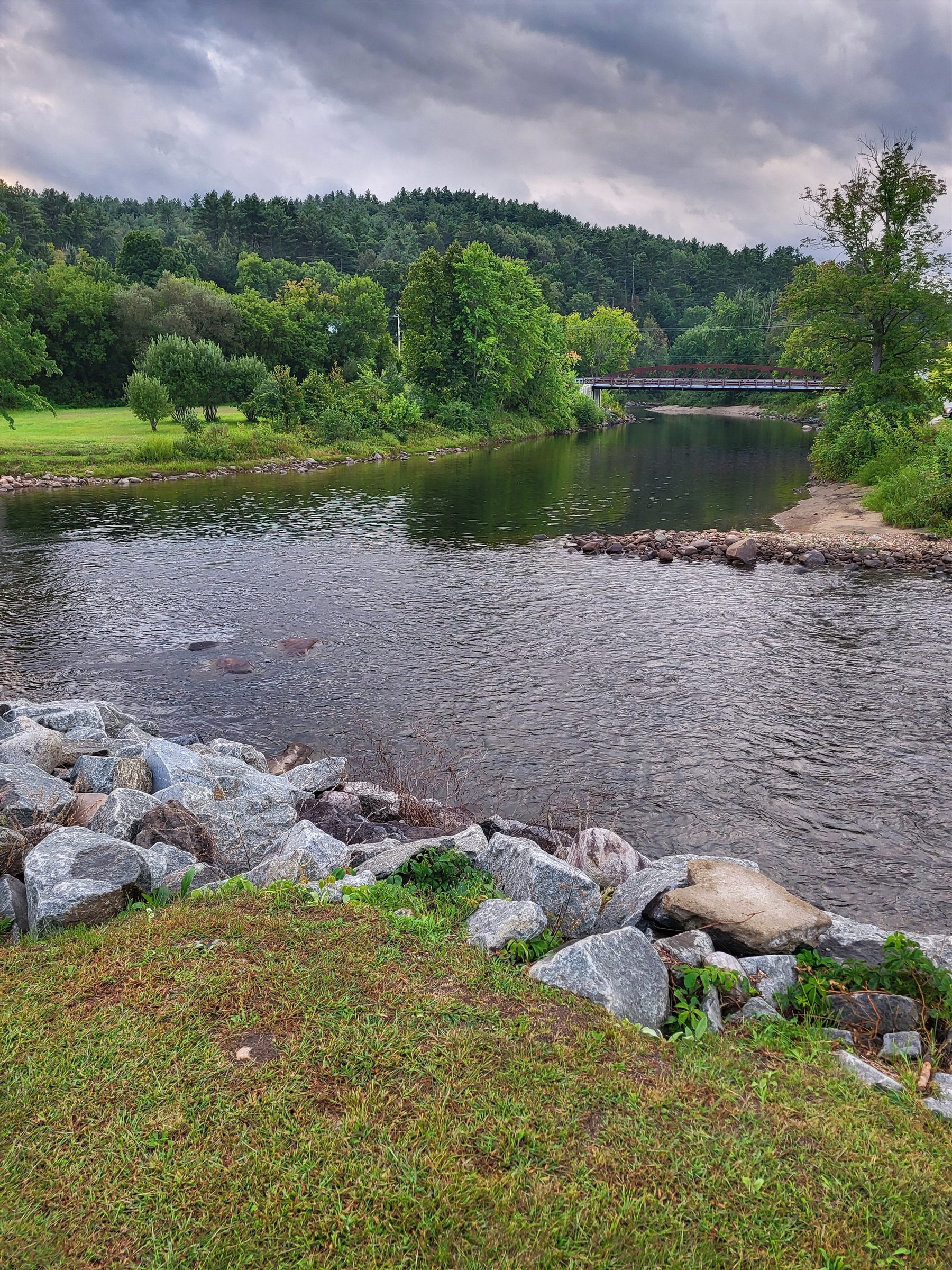 A calm river and distant bridge beneath dramatic storm clouds